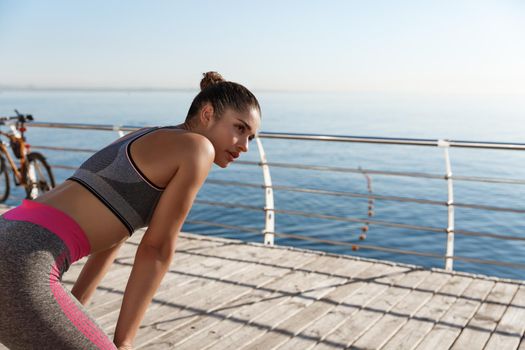 Rear view of determined sportswoman taking a breath after running along seaside promenade
