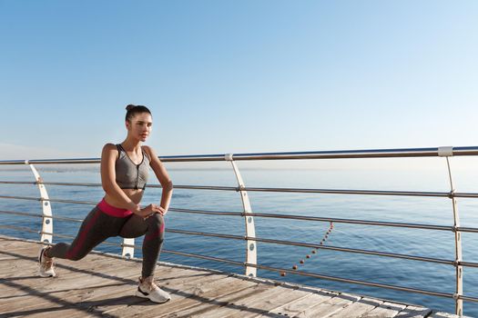 Outdoor shot of smiling fitness woman stretching and working out on the seaside promenade