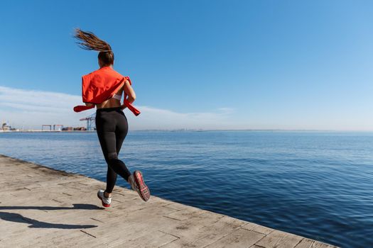 Rear view of sportswoman running along the seaside promenade. Fitness woman jogging near sea