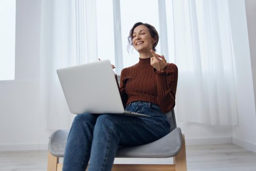 Smiling enjoyed conversation in video call conference with boyfriend cheerful curly woman sit in chair with laptop on knees at home. Distance remote communication concept. Copy space for ad