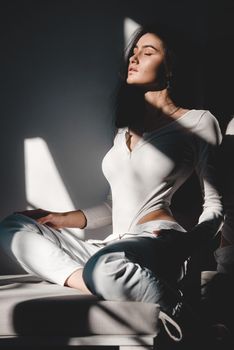portrait of beautiful gentle woman in a white bodysuit posing in the sunshine. Black long hair. sensuality and tenderness