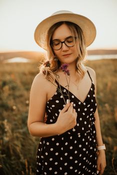 woman in a dress with polka dots in a hat walks through the meadow