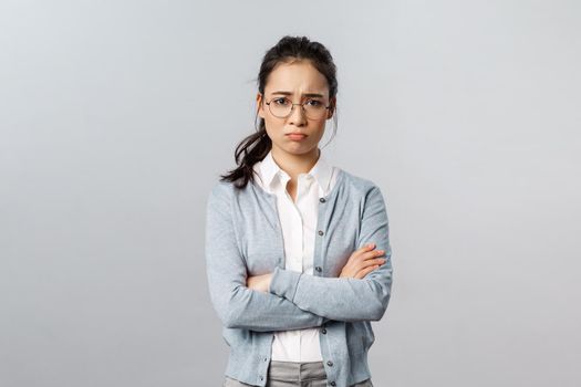 Portrait of offended insecure and timid cute asian girl complaining on cruel customer being rude to her, cross hands over chest defensive and upset, frowning gloomy, feel upset grey background