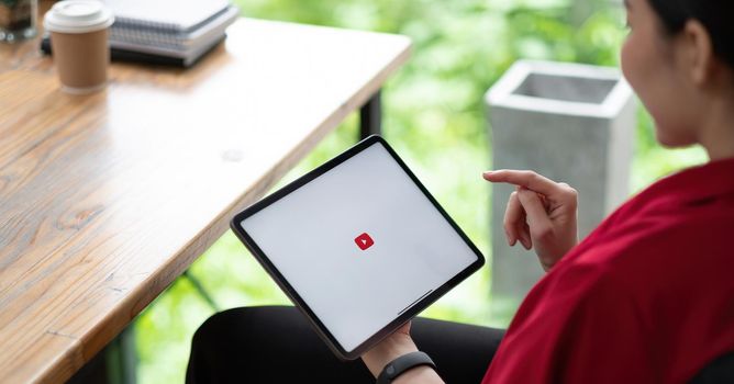 CHIANG MAI, THAILAND - AUG 01, 2021 : Woman hand holding and is pressing the Youtube screen on apple digital tablet, YouTube is the popular online video-sharing website.