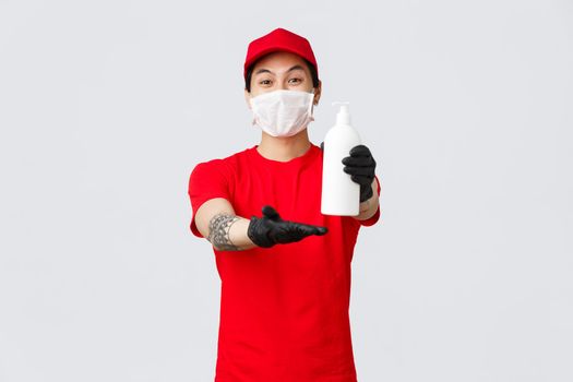 Delivery service worker giving client hand sanitizer. Cheerful courier hold sanitizer, wear medical mask and protective gloves during covid-19 self-quarantine, deliver orders in pandemic