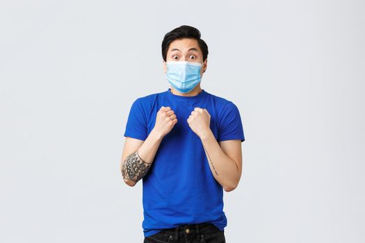 Different emotions, social distancing, self-quarantine on coronavirus and lifestyle concept. Excited and shocked, startled asian man in blue t-shirt, clench fists and looking with anticipation