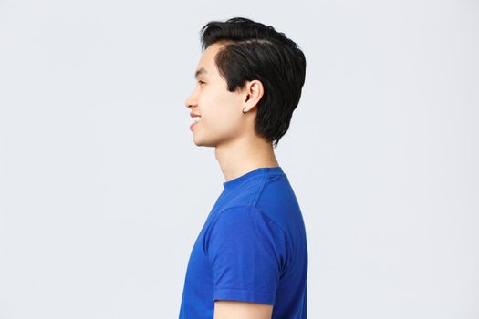 Lifestyle, people emotions and beauty concept. Profile shot of asian hipster guy with earring in blue t-shirt, smiling satisfied after making good new hairuct, hairstyle at barbershop