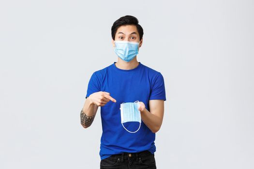 Different emotions, social distancing, quarantine on coronavirus and lifestyle concept. Excited asian man in protective equipment, pointing finger at medical mask, recommend wear it during covid-19