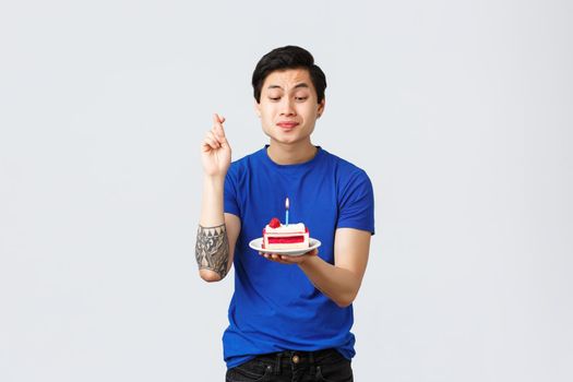 Self-quarantine, home lifestyle and celebration concept. Excited happy asian guy, want dream come true, looking at b-day cake, lit candle on birthday, cross fingers making wish.