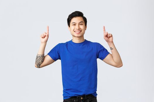 Different emotions, people lifestyle and advertising concept. Cheerful handsome asian man in blue t-shirt pointing fingers up. Guy advertising and inform about new promo, smiling camera