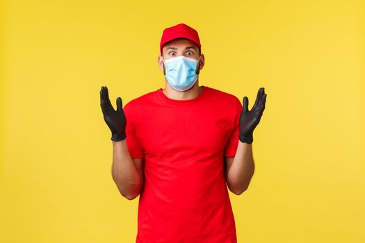 Express delivery during pandemic, covid-19, safe shipping, online shopping concept. Impressed and startled courier in red uniform cap, t-shirt raise hands astonished, wear medical mask