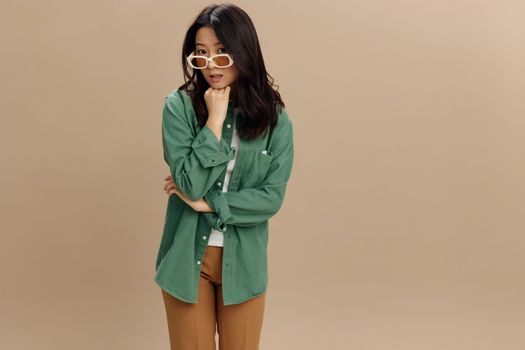 Oops. Upset pensive cute Korean young woman in khaki green shirt stylish eyewear recline on fist posing isolated on over beige pastel studio background. Cool fashion offer. Sunglasses ad concept