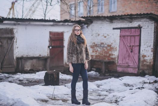 Girl blonde in cat eyes glasses in an artificial faux fur coat in winter