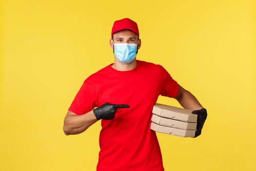 Food delivery, tracking orders, covid-19 and self-quarantine concept. Smiling courier pointing at delicious pizza, bring order to customer home, wear protective gloves and medical mask