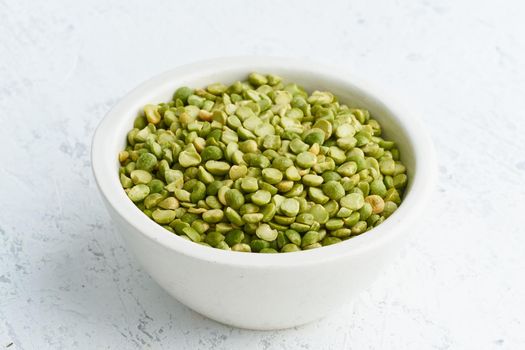 Green peas in white bowl on white background. Dried cereals in cup, vegan food. Side view