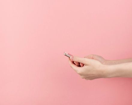 Young female hand holds smartphone on pastel pink background copy space
