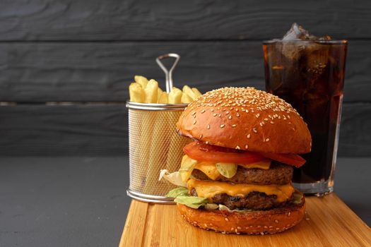 Delicious burger and fries on wooden board against black background