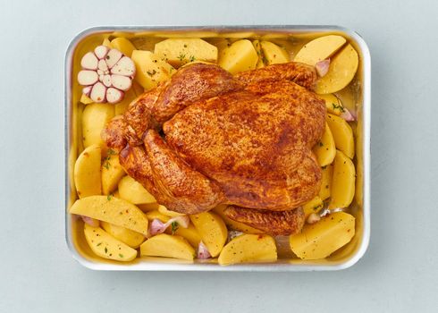 whole marinated chicken in sauce with raw potatoes in baking dish