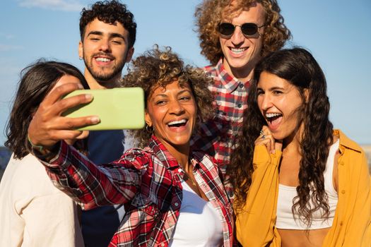 Smiling young multiracial friends take selfie together using smartphone outdoors