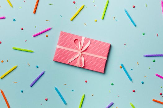 wrapped gift box around colorful candles sprinkles blue backdrop