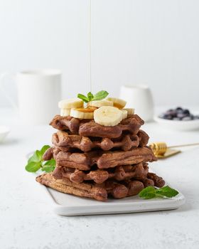 Chocolate banana waffles with maple syrup on white table, side view, vertical. Sweet brunch