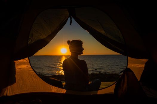 A woman and a dog in a tourist tent at sunrise. Camping with a pet