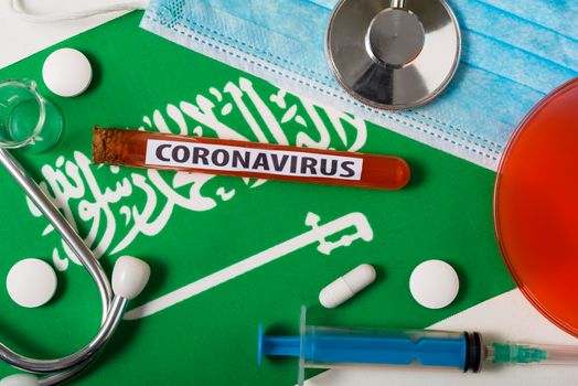 Coronavirus, nCoV concept. Top view protective breathing mask, stethoscope, syringe, tablets on the flag of Saudi Arabia.