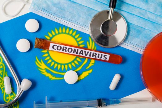 Coronavirus, nCoV concept. Top view protective breathing mask, stethoscope, syringe, tablets on the flag of Kazakhstan.