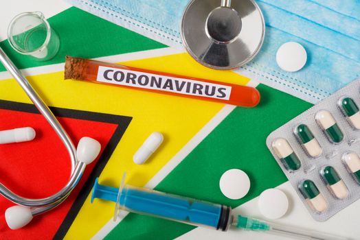 Coronavirus, nCoV concept. Top view protective breathing mask, stethoscope, syringe, pills on the flag of Guyana.