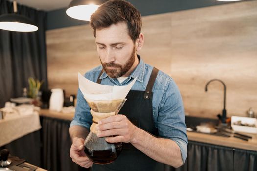 Handsome barista with stylish beard smelling filter coffee in cafeteria