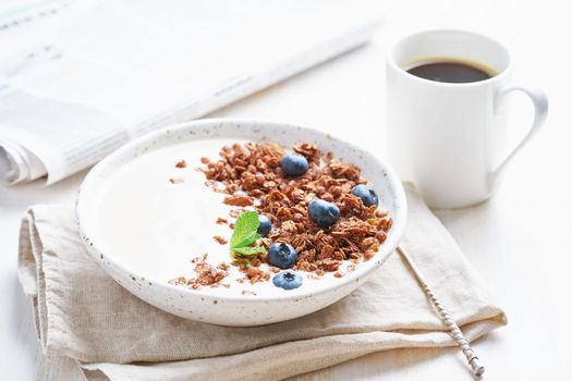 Breakfast with cup of coffee, newspaper, yogurt with chocolate granola