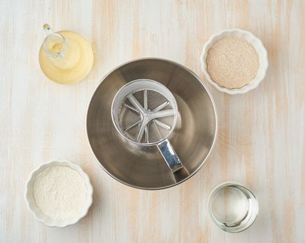 Background with ingredients for dough, bowl and sieve. Top view, white wooden table
