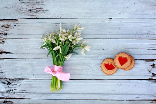 Snowdrops with pink ribbon and biscuit on wooden background