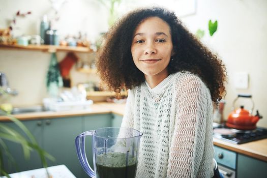Shot of a young woman smiling at camera while making a healthy smoothie at home