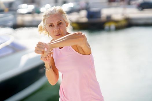 Elderly female doing shadow boxing outdoors. Senior woman doing sport in a coastal port