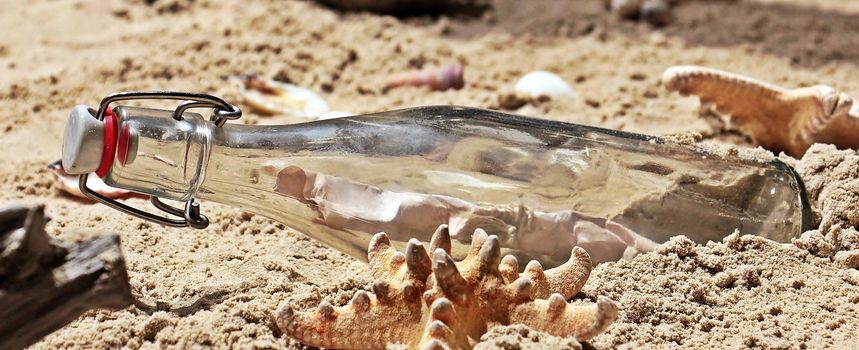 Summer sandy beach concept with letter in bottle, starfish and shells.