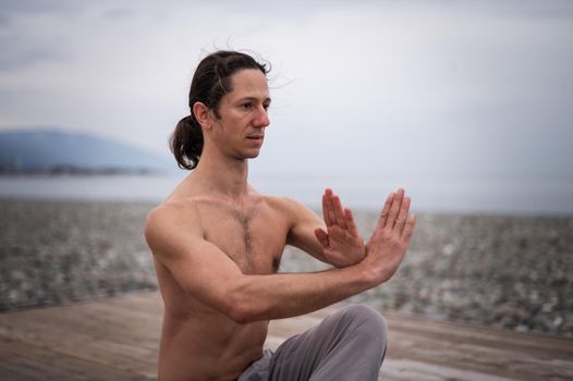 Caucasian man with naked torso practicing wushu on the seashore.