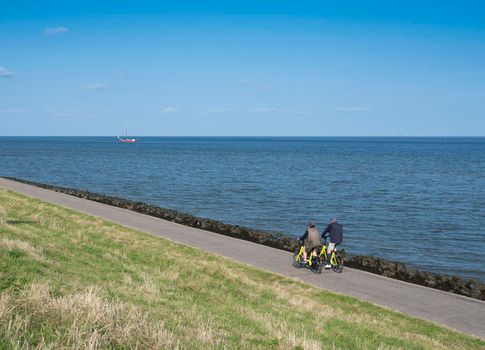 couple rides bicycle on dike of wadden sea on dutch island of texel in summer
