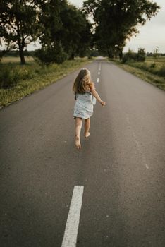 European girl in a blue dress runs away along a clean asphalt road