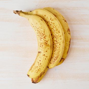 Ripe bananas with brown spots on bright white wooden table
