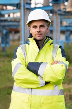 Portrait of industrial worker on power electric station. Portrait of happy male engineer in protective helmet crossing arms while looking to camera