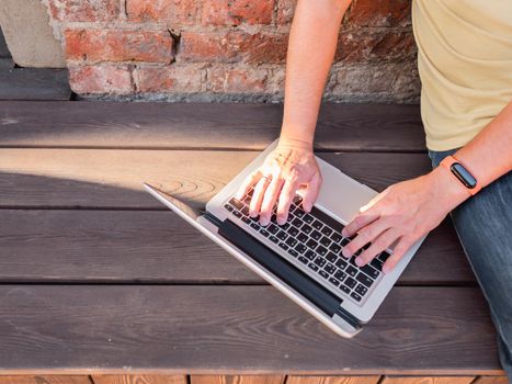Top view on man's hands on computer keyboard. Freelancer works outdoors with laptop. Modern lifestyle. Open air workplace.