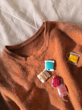 Top view on earth toned wool sweater and coils of colorful embroidery threads. Remaking old clothes. DIY. Handmade craft.