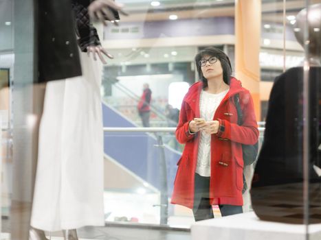 Woman stares on dummies in clothing store. Casual outfit hanging on mannequins. View through transparent shop window. Shopping at mall. Basic clothes for everyday wear. Modern urban fashion.