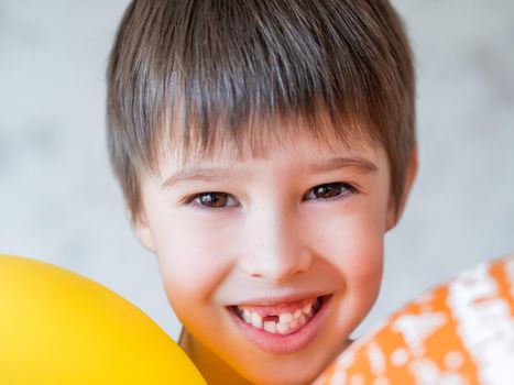 Smiling kid shows hole in row of teeth in his mouth. One incisor fell out just now. Happy child with air balloons.
