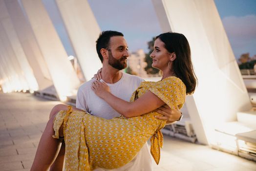 A man with a beard is holding his girl in a yellow dress in his arms in Valencia