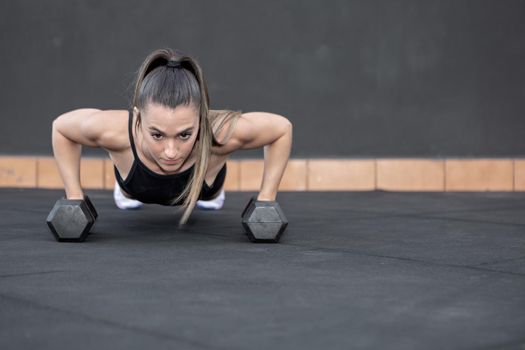 Sportswoman doing push ups on dumbbells