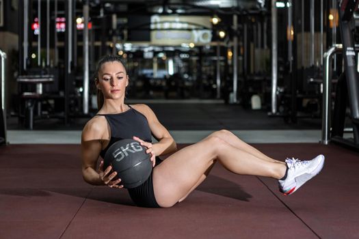 Muscular sportswoman doing side twist with medicine ball in gym