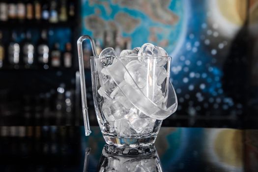 Chilled ice cookware with ice cubes and plastic tongs on the bar counter