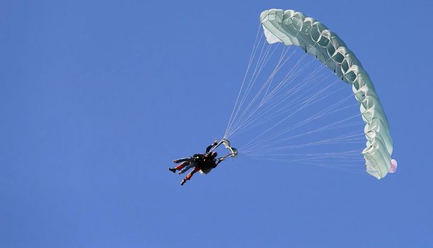 A skydiver with a white parachute canopy against a blue sky and white clouds, close-up.